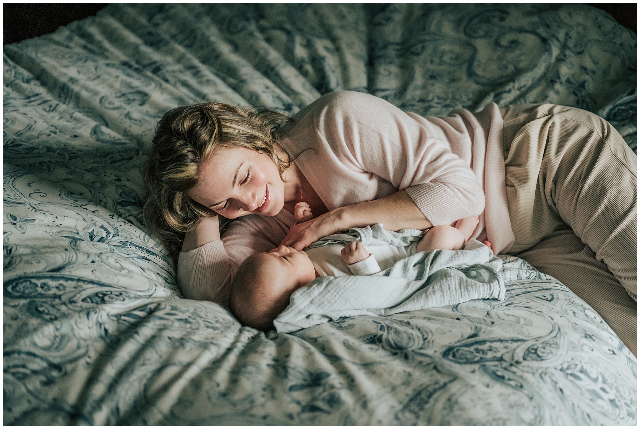 A photo of a young mom snuggling with her newborn baby on a bed during their photography session in the Boston area.