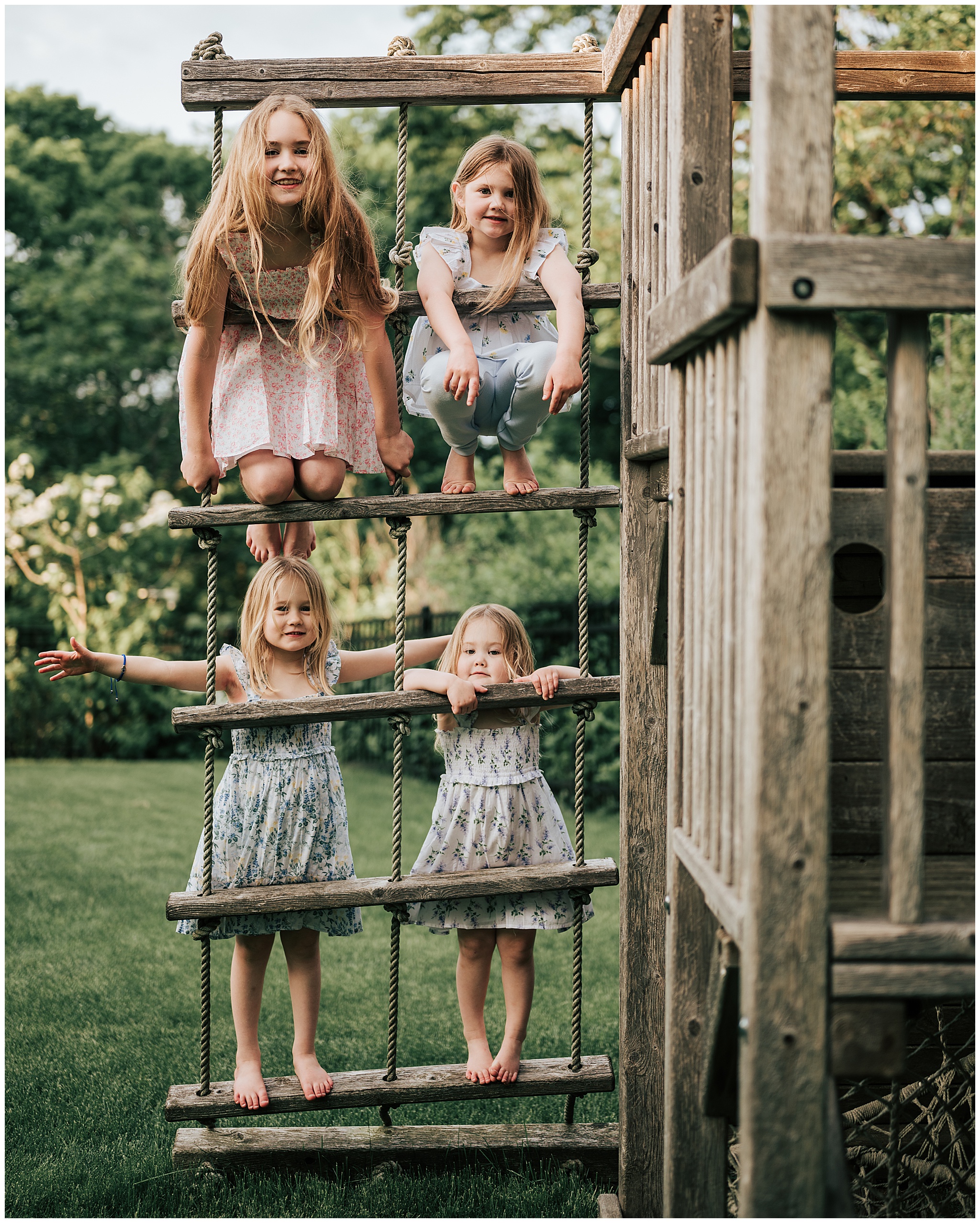 Four little girls (all sisters) standing on the rope ladder of a playground set in their Boston-area back yard during a family photography session.