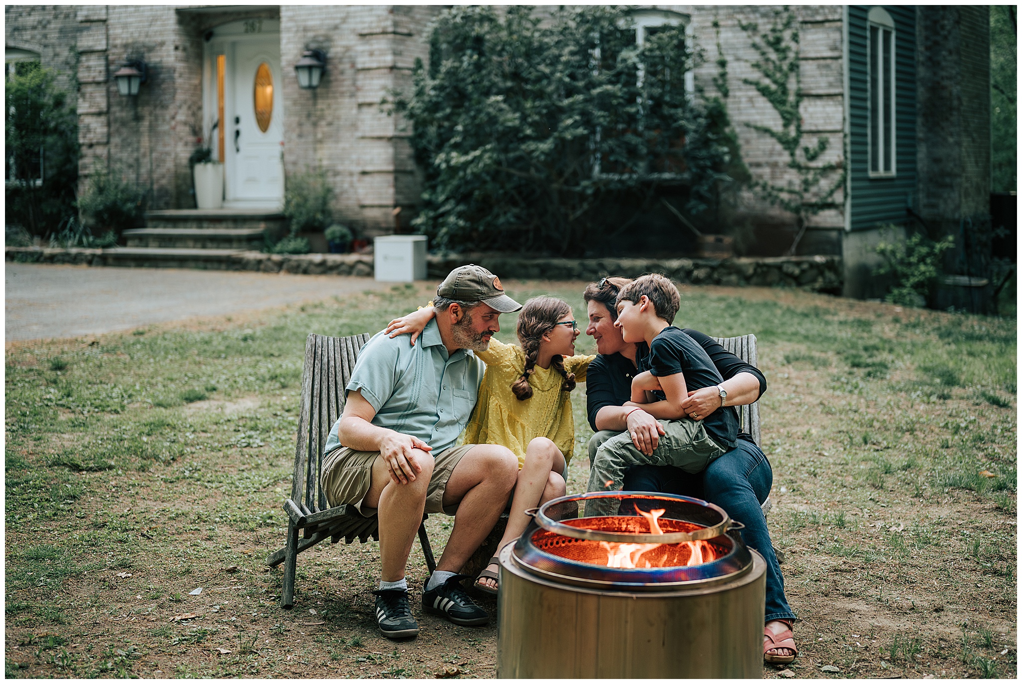 A smiling family sitting outside their house in front of a fire pit during a photography session outside of Boston.